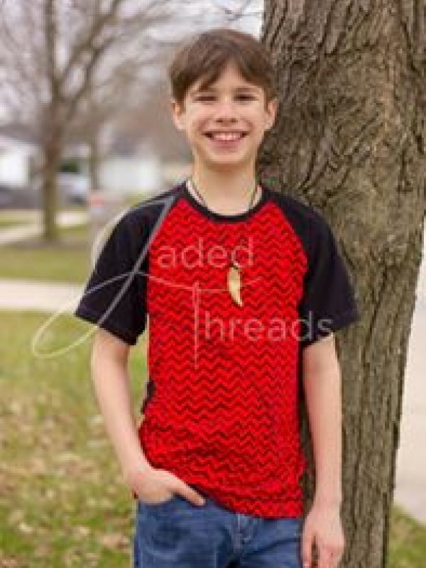 A tween boy with brown hair smiles while looking at the camera. He has his hand