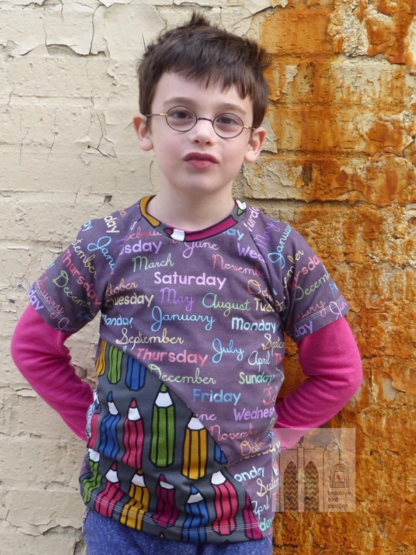 Boy standing in front of a distressed brick wall. He is almost smiling. He wears